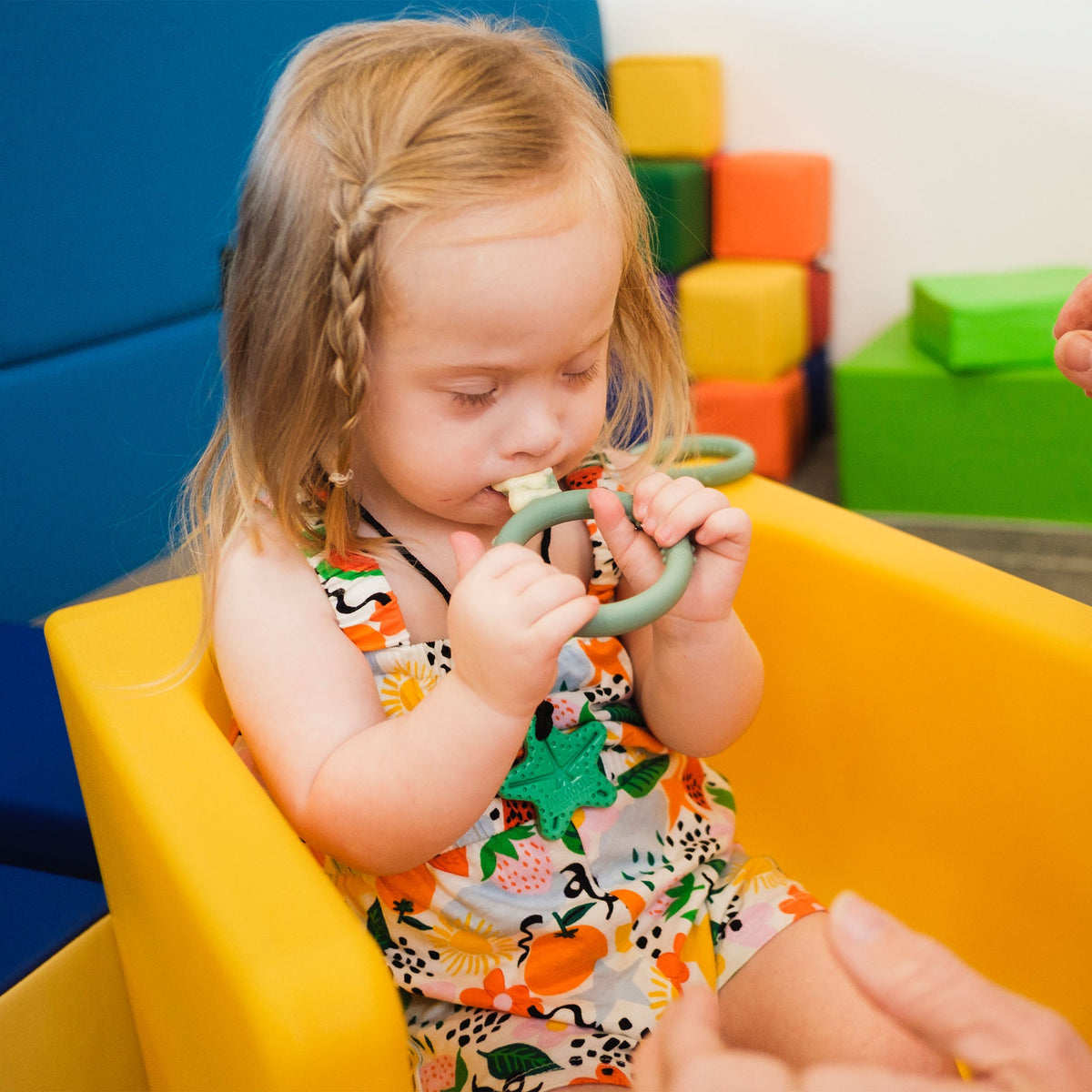A child holding a TalkTools Itsy Rings spoon while seated in a high chair