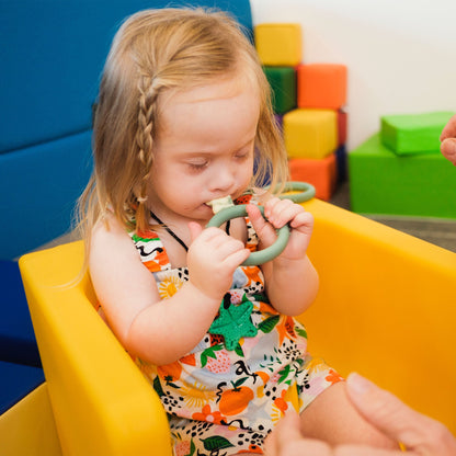 A child holding a TalkTools Itsy Rings spoon while seated in a high chair